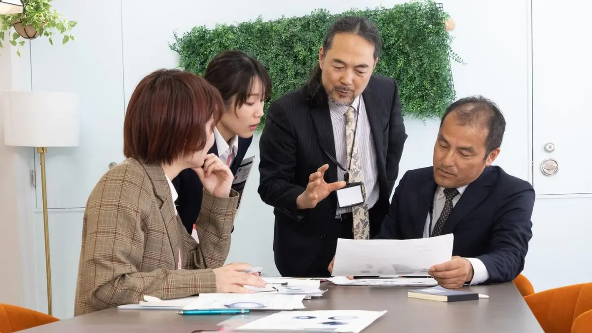資料を囲んで商談する日本人の企業担当者（支援業種のイメージ）